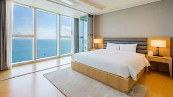 Habitación de hotel moderna con una cama grande, dos mesitas de noche con lámparas, vistas al mar y un ventanal amplio.