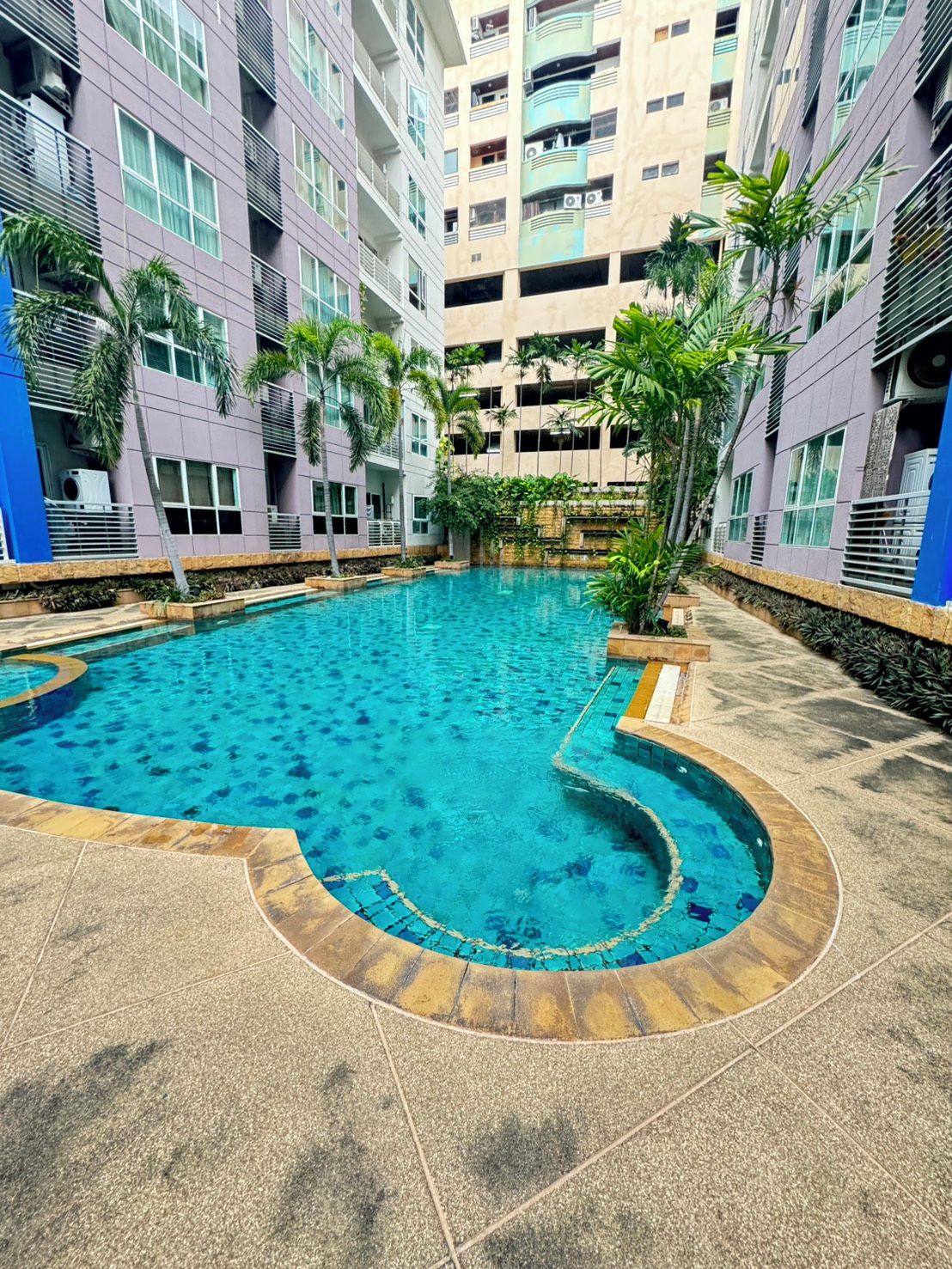 Une piscine au design incurvé, entourée d’un bâtiment à plusieurs étages doté de balcons.