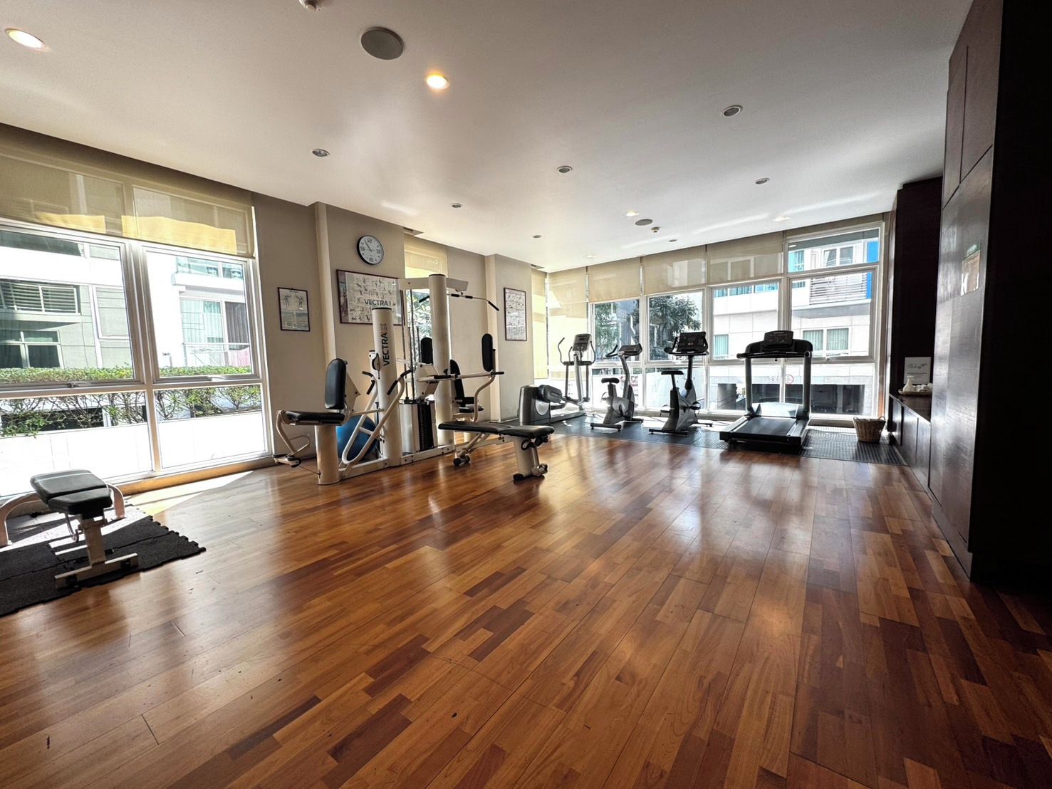 A gym with exercise equipment, large windows, and a wooden floor.