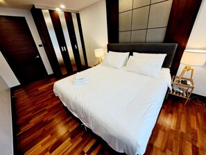 A hotel room with a large bed, wooden flooring, a dark headboard, two bedside lamps, and a wardrobe with vertical stripes. - Luxurious 2-Bedroom Condo with Pool View near BTS Ekkamai Station (Khwaeng Khlong Tan Nuea)
