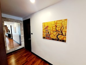 A hallway with a wooden floor, a white wall, and a single piece of abstract art. - Luxurious 2-Bedroom Condo with Pool View near BTS Ekkamai Station (Khwaeng Khlong Tan Nuea)