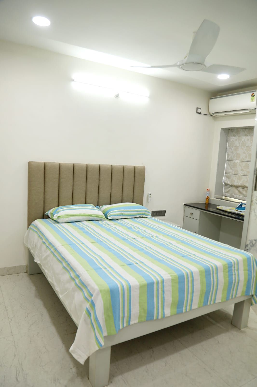 Une chambre à coucher avec un lit, une table de chevet, un miroir et un ventilateur de plafond.