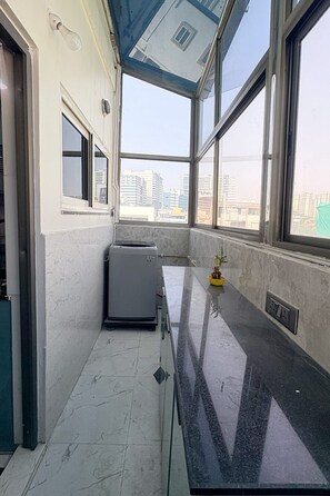 A room with a large window, a small refrigerator, and a yellow plant on the windowsill. - Miron Hotels & Resorts (Hyderabad)