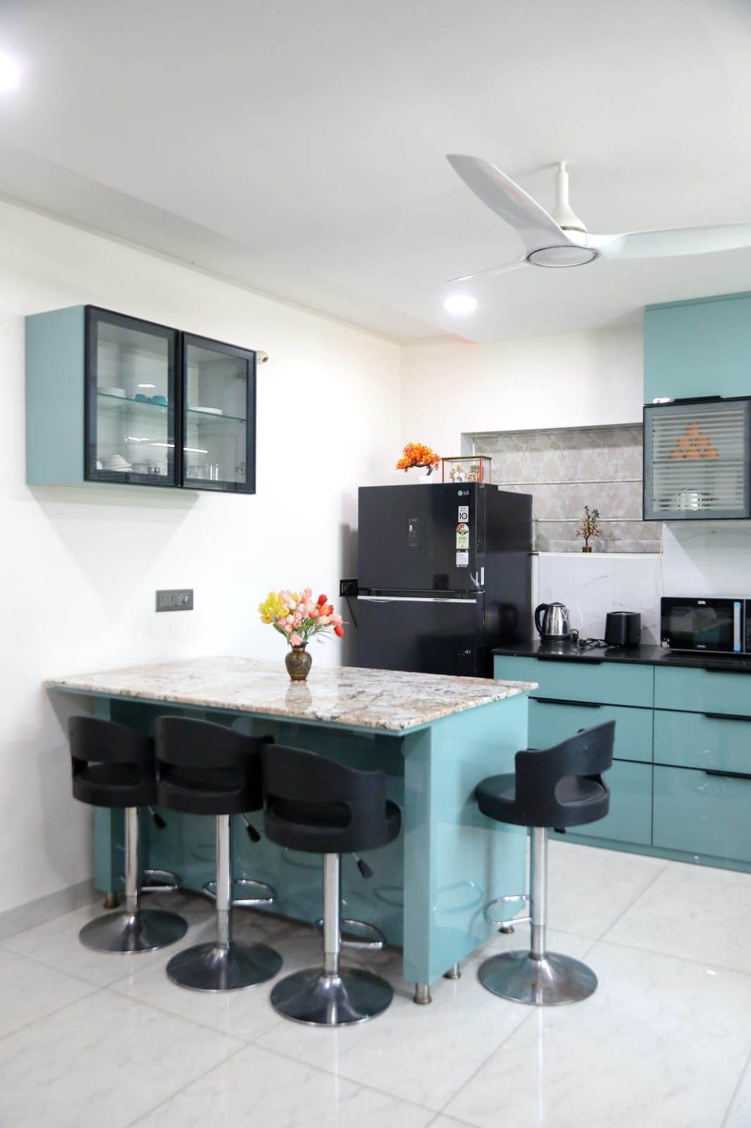 Una cocina moderna con encimera de mármol, taburetes negros, refrigerador negro y armarios color esmeralda.