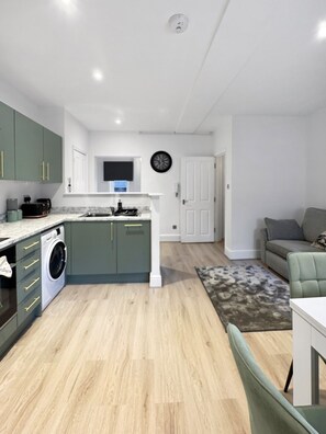 Una cocina moderna con lavadora incorporada, un comedor con mesa y sillas, y una sala de estar con sofá.
