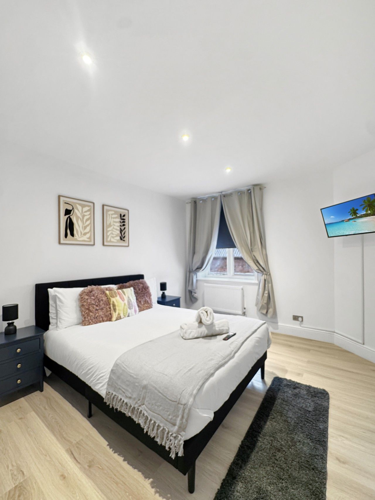 Une chambre à coucher moderne, avec un lit, des tables de chevet, un téléviseur à écran plat et des œuvres d’art accrochées au mur.