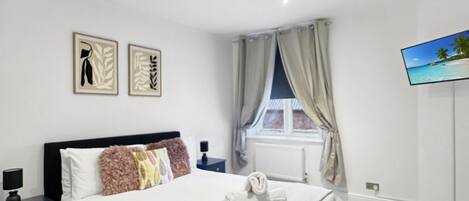 Een moderne slaapkamer met een bed, nachtkastjes, een flatscreen-tv en kunst aan de muur.