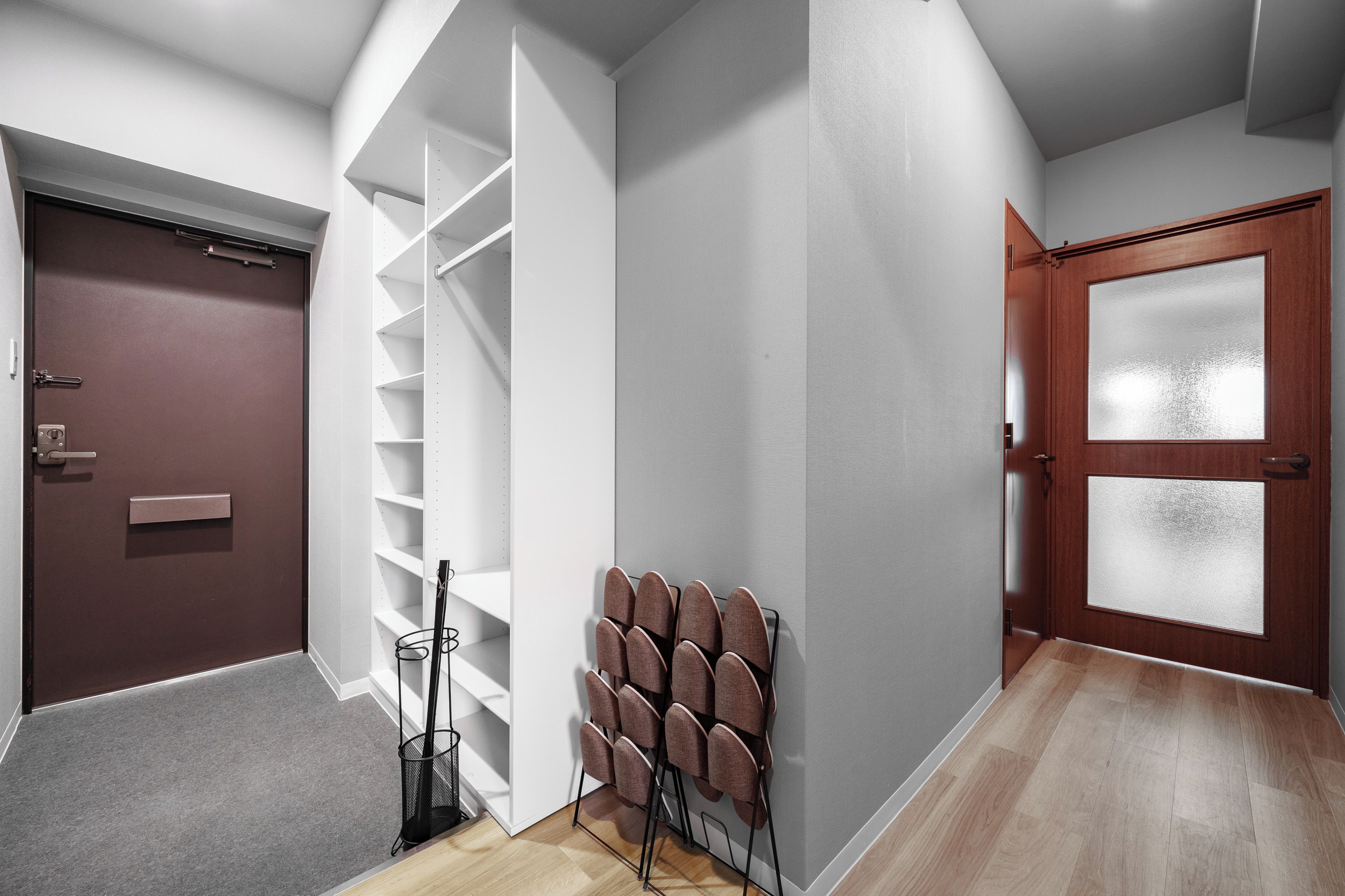 A hallway with a brown door, a white wall with a built-in shelf, and a wooden door with frosted glass panels.