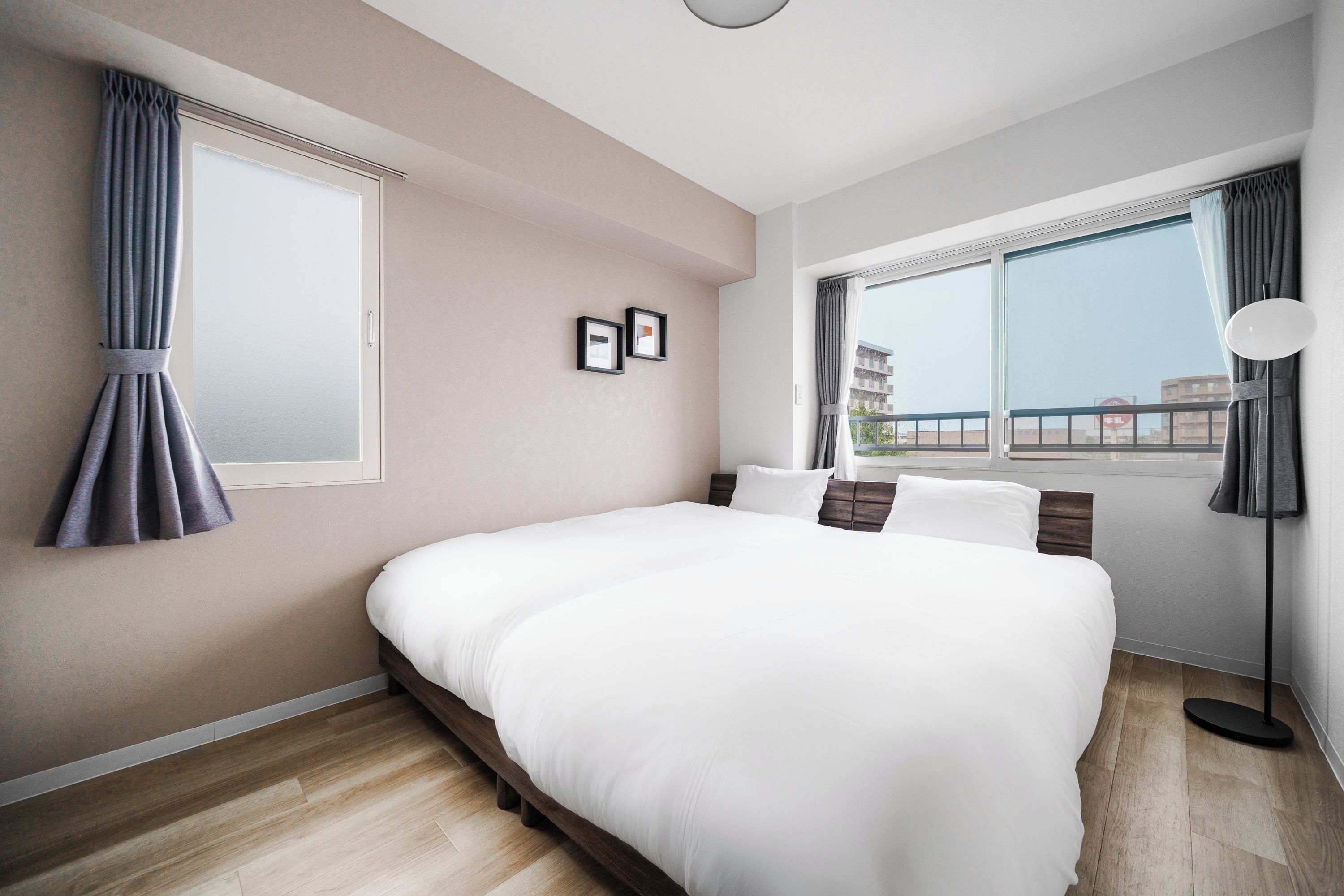 A modern hotel room with a large bed, a window with curtains, a bedside lamp, and a view of the city.