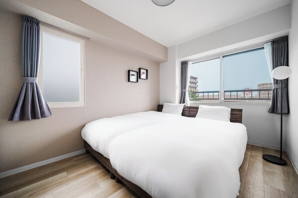 A modern hotel room with a large bed, a window with curtains, a bedside lamp, and a view of the city.