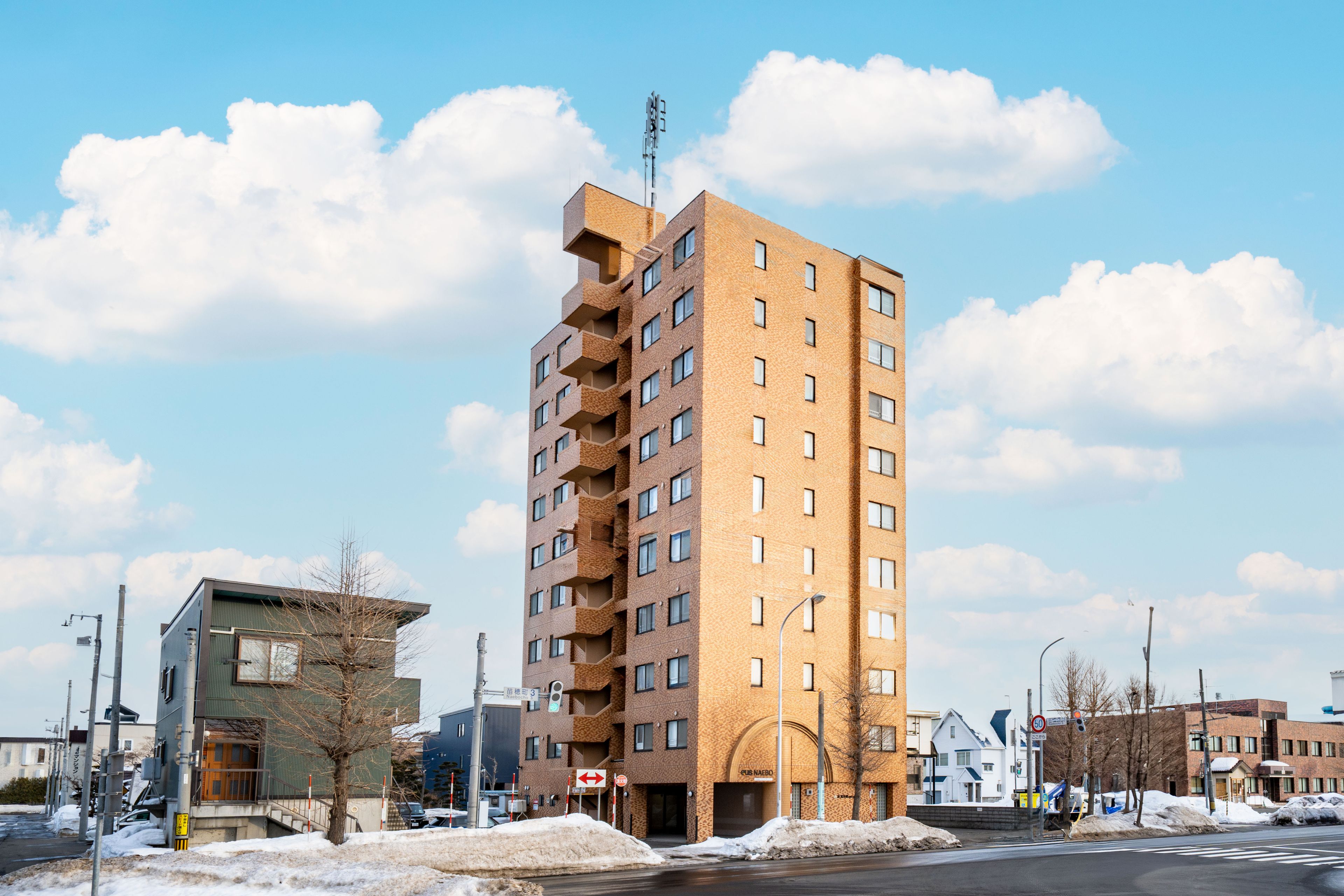 A multi-story building with a modern architectural design, featuring balconies and a prominent antenna.