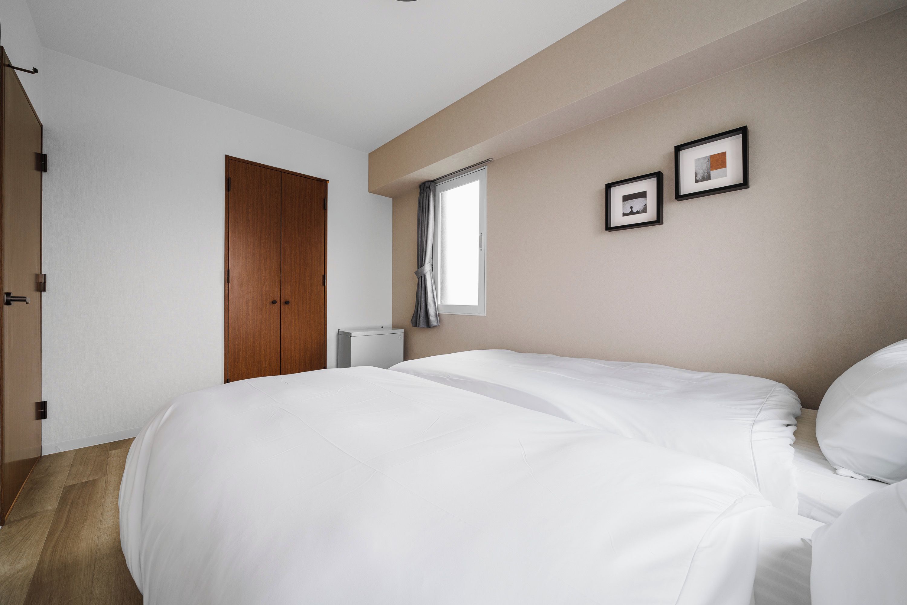 A bedroom with a large bed, a wardrobe, a window with curtains, and two framed pictures on the wall.