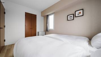 A bedroom with a large bed, a wardrobe, a window with curtains, and two framed pictures on the wall.