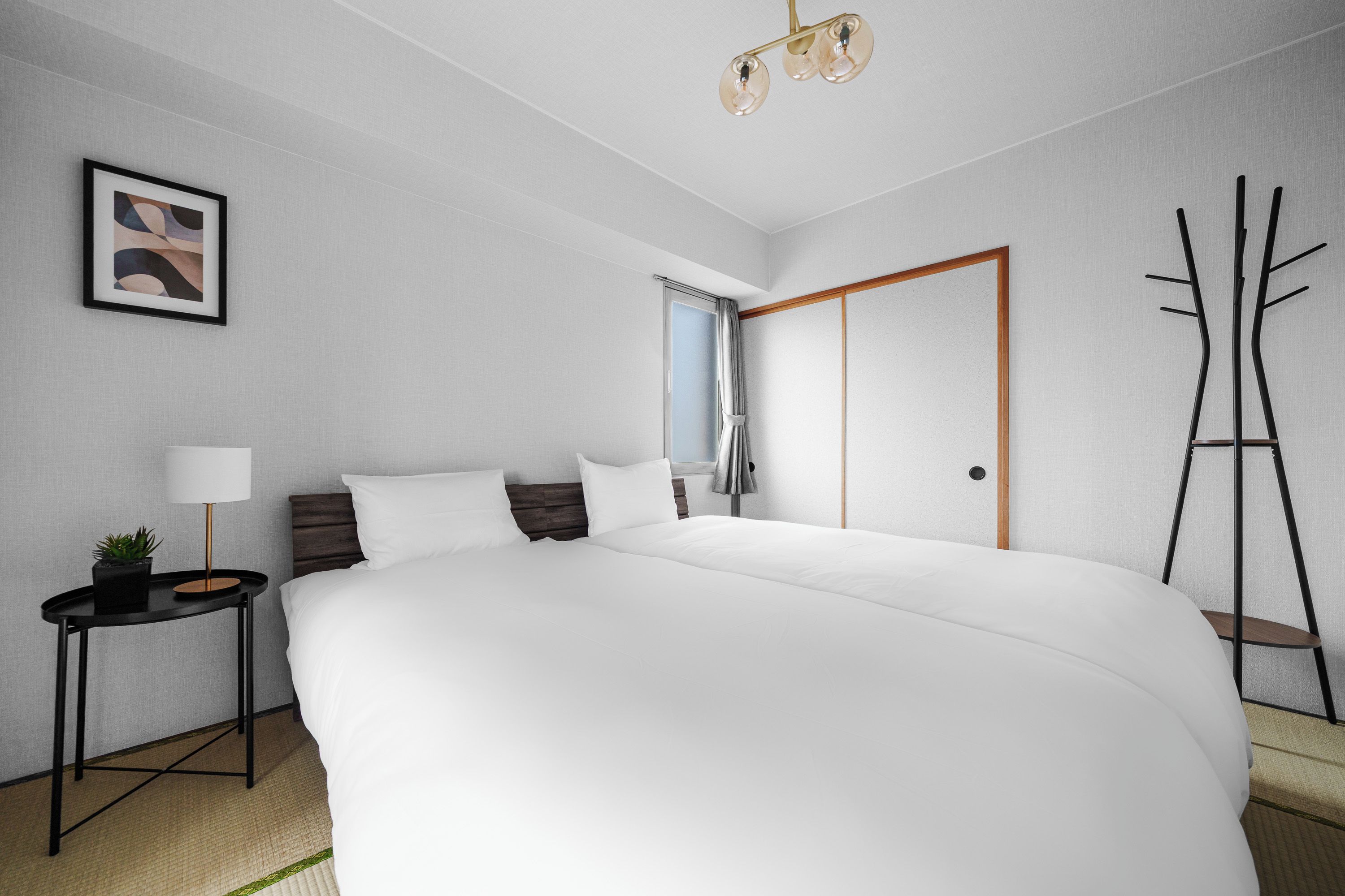 Een moderne hotelkamer met een groot bed, een nachtkastje met een lamp, een lijst met een afbeelding aan de muur, en een kledingkast.
