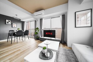 A modern living room with a flat-screen TV displaying 'NETFLIX,' a dining area with a table and chairs, and a sofa.