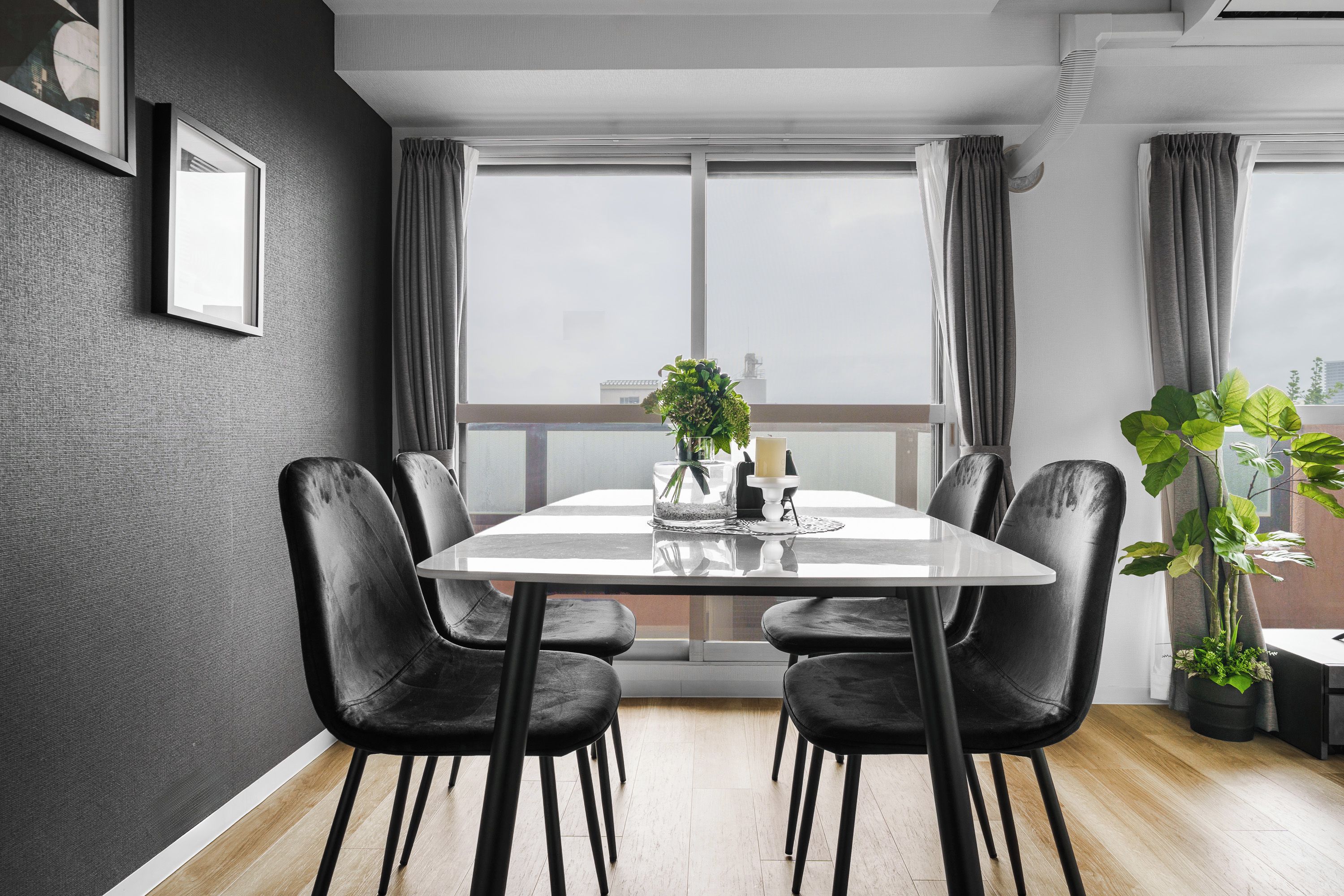 A modern dining room with a rectangular table, black chairs, and a large window with curtains.