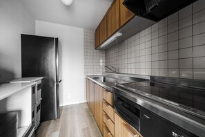 A modern kitchen with a stainless steel refrigerator, wooden cabinets, a black range hood, and a tiled backsplash.