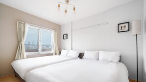 A hotel room with two beds, a large window with curtains, a floor lamp, and a framed picture on the wall. - E-US Naebo 403 (Sapporo)