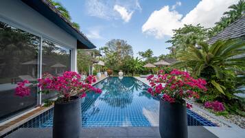 Una piscina con borde de azulejos, rodeada de plantas en macetas y mobiliario exterior.