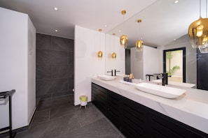 Casa de banho moderna com lavatório branco, armários pretos e um espelho grande.
