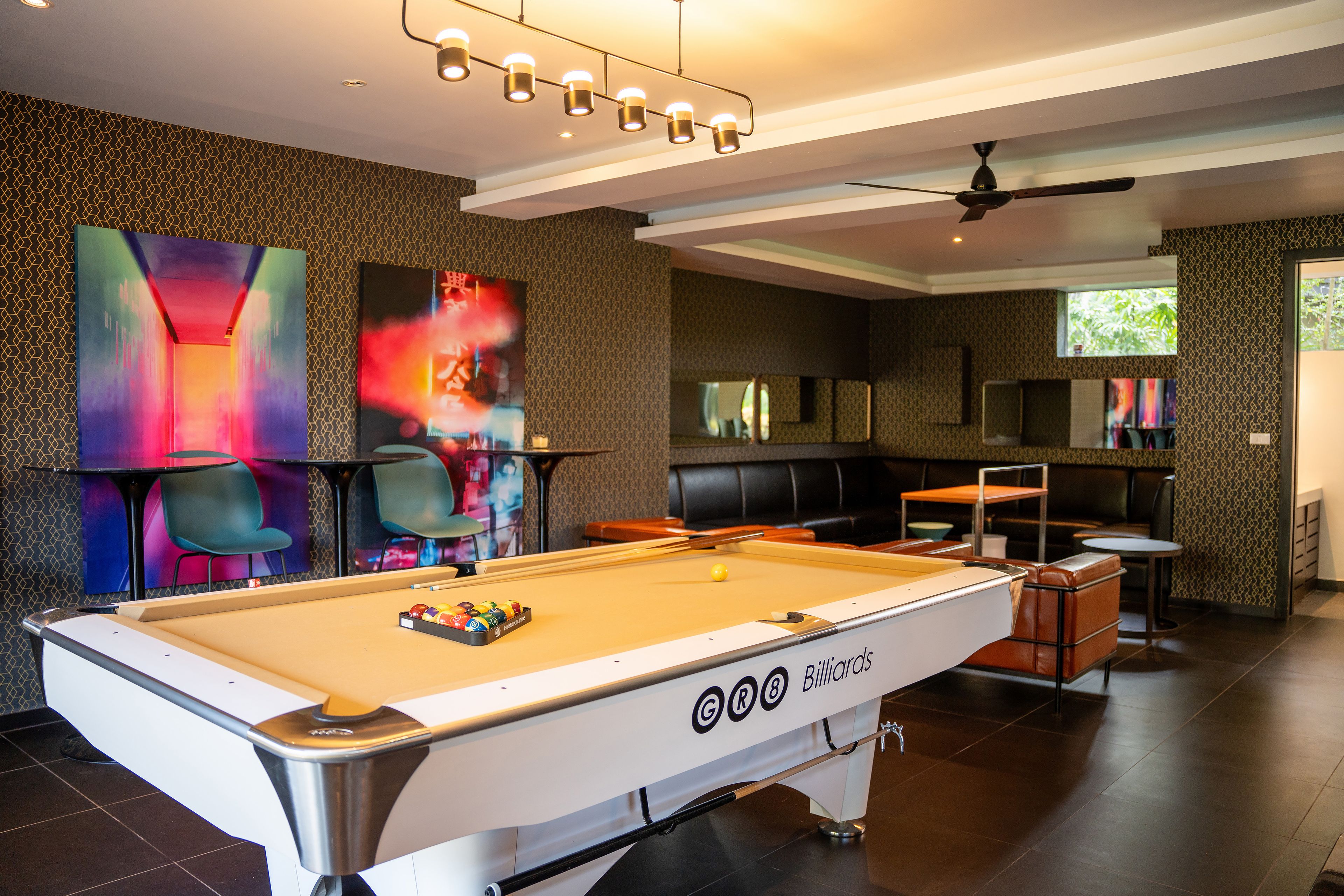 A billiards table with a pool cue rack, a ceiling fan, and a seating area with chairs and tables.