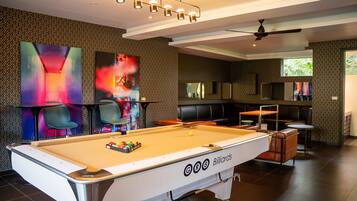 A billiards table with a pool cue rack, a ceiling fan, and a seating area with chairs and tables.