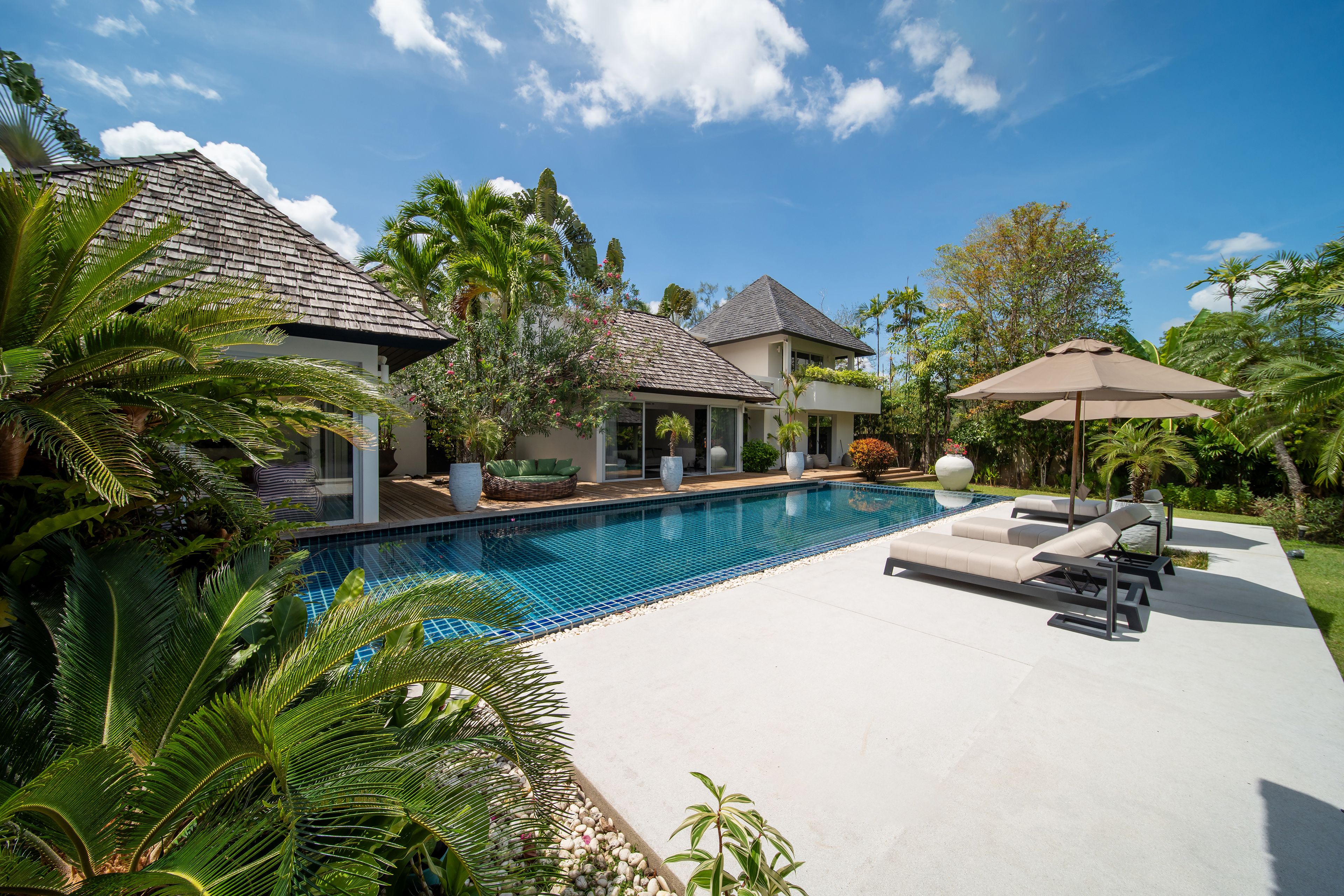 A residential property with a swimming pool, lounge chairs, and tropical vegetation.