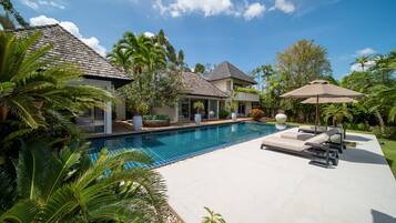 A residential property with a swimming pool, lounge chairs, and tropical vegetation.