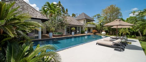 A residential property with a swimming pool, lounge chairs, and tropical vegetation.