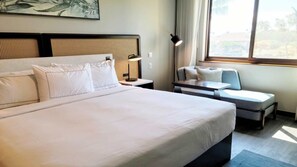 Habitación de hotel con una cama grande, un sofá pequeño, una mesita de noche con lámpara y una ventana con vistas.