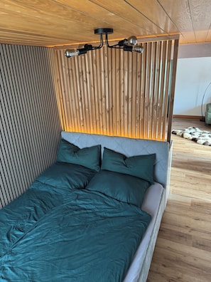 A bed with a headboard featuring vertical wooden slats and a modern light fixture above it.