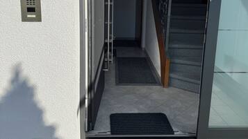 Ein moderner Hauseingang mit Glastür, einem Metall-Sprechanlage und einer sichtbaren Innentreppe.