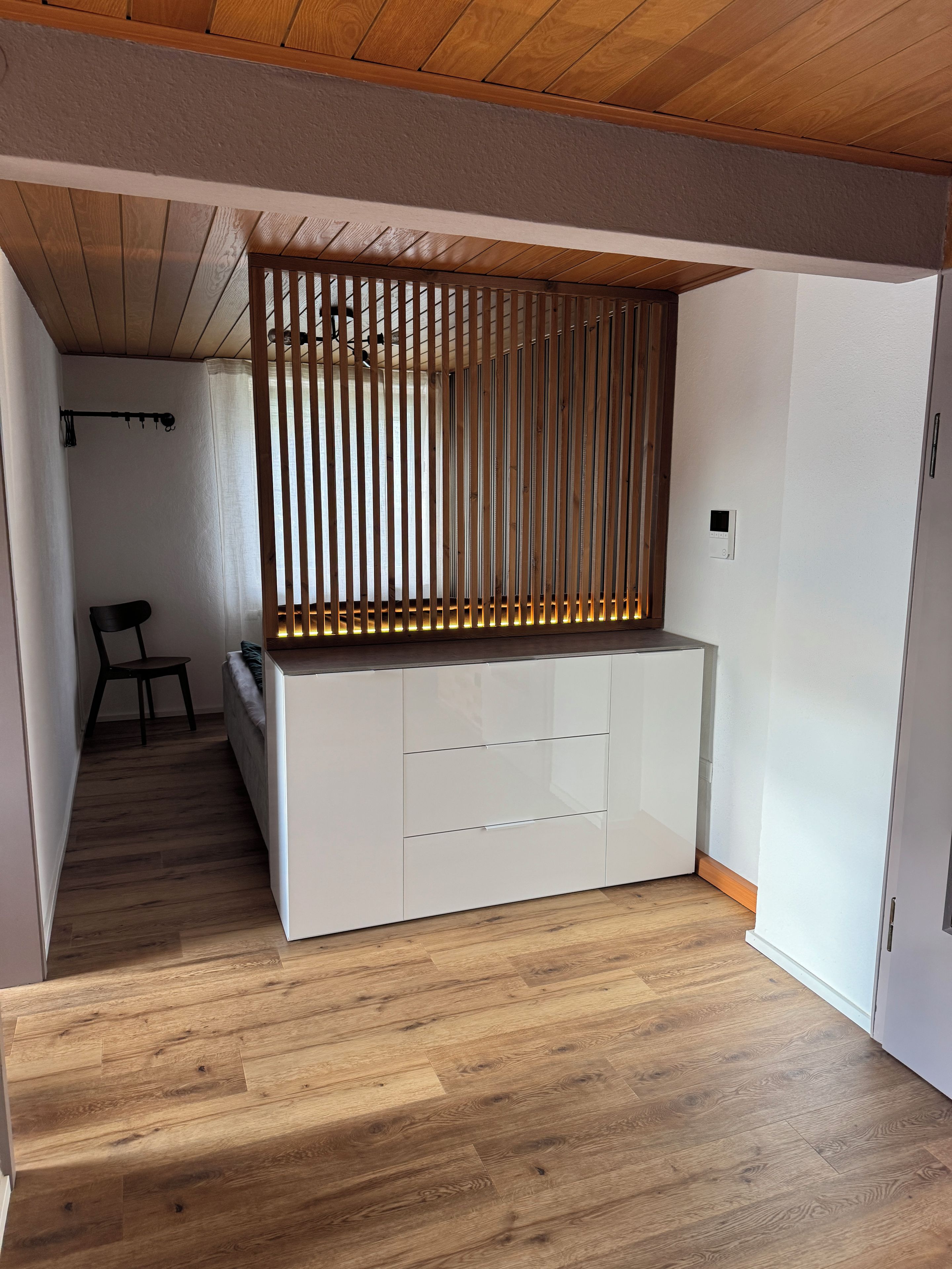 Ein modernes Interieur mit Holzboden, einer weißen, eingebauten Sitzbank mit Schubladen und einer Raumtrennung aus Holzlatten.