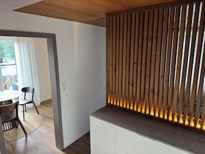 Un interior moderno con un separador de listones de madera, una mesa redonda con sillas y un armario blanco.