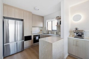 A modern kitchen with stainless steel appliances, a central island, and light wood cabinetry. - Design-Led Escape – Bondi & Tamarama – 2BR with Ocean Views (Bondi)