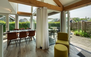A modern dining area with a table set for four, large windows, and a view of the backyard. - Zonnedorp 13 villa for seaside holidays near the beach (Renesse)