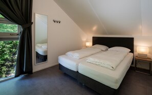 Ein modernes Schlafzimmer mit einem großen Bett, einem Nachttisch mit Lampe, einem Spiegel und Blick ins Grüne.