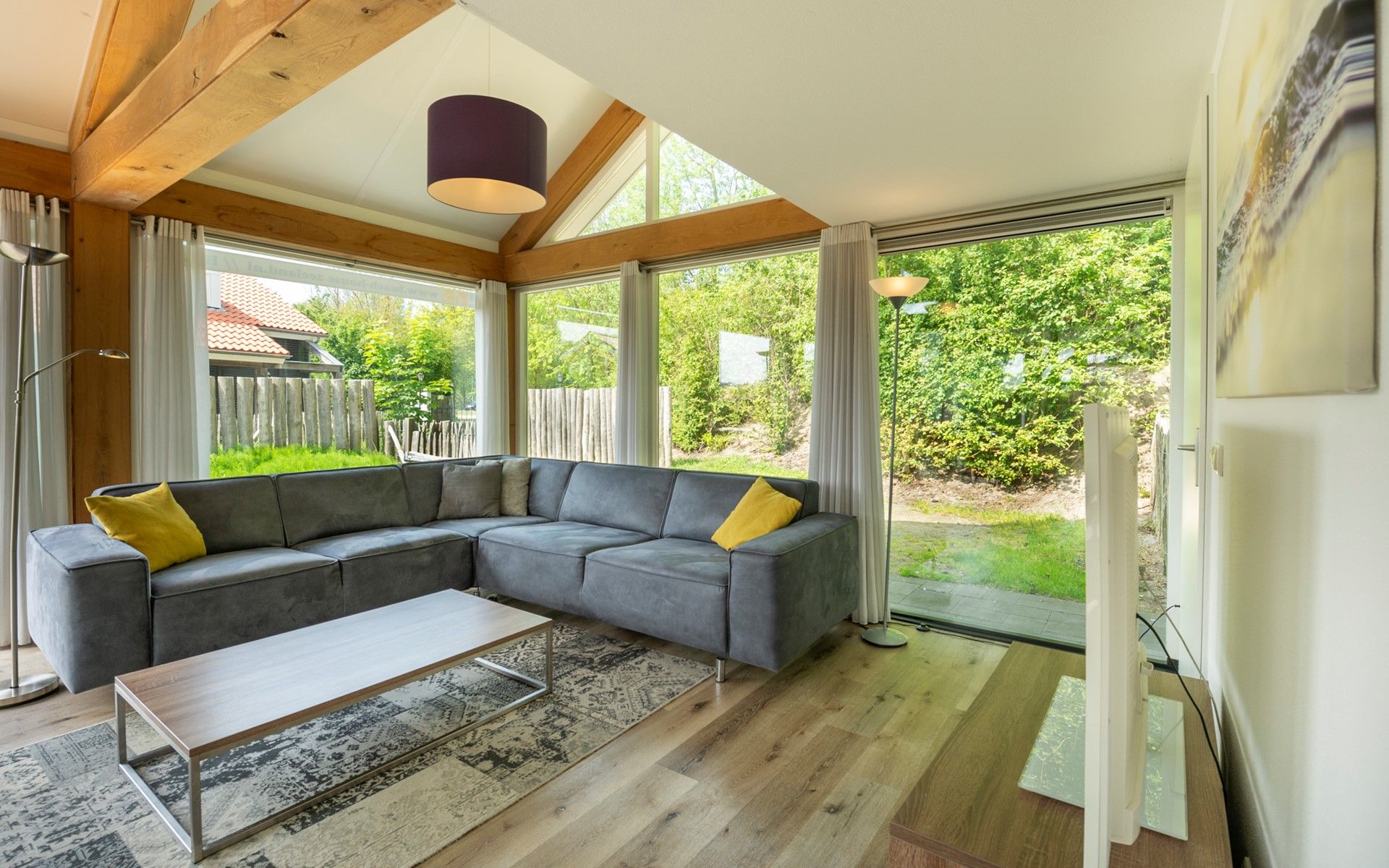 A modern living room with a sectional sofa, a coffee table, and a view of the outdoors through large windows.