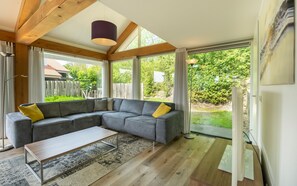 Ein modernes Wohnzimmer mit einem Ecksofa, einem Couchtisch und Blick ins Freie durch große Fenster.