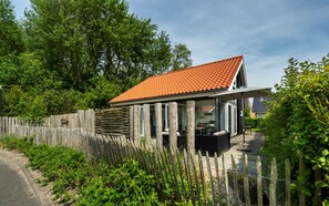 A modern house with a tiled roof, a wooden fence, and a patio area. - Zonnedorp 13 villa for seaside holidays near the beach (Renesse)