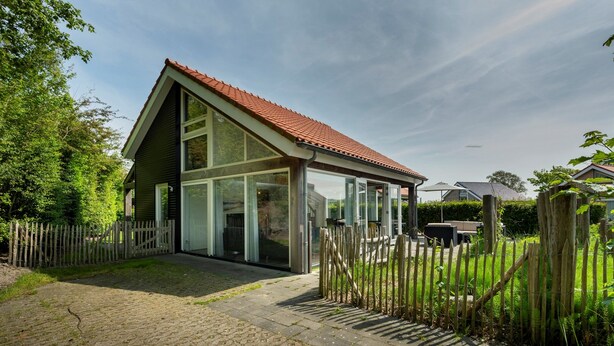 Een modern huis met een schuin dak, grote ramen en een houten omheining.