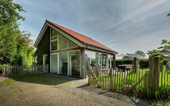 A modern house with a sloped roof, large windows, and a wooden fence. - Zonnedorp 13 villa for seaside holidays near the beach (Renesse)