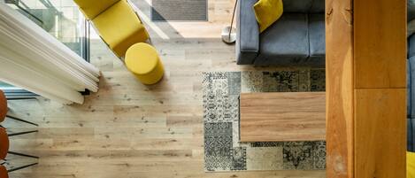 Een modern interieur met een houten vloer, een kamerkleed met patroon, een bank met kussens en een gele fauteuil.