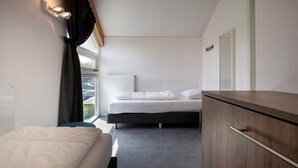Een moderne hotelkamer met een bed, nachtkastje, kledingkast en raam met gordijnen.