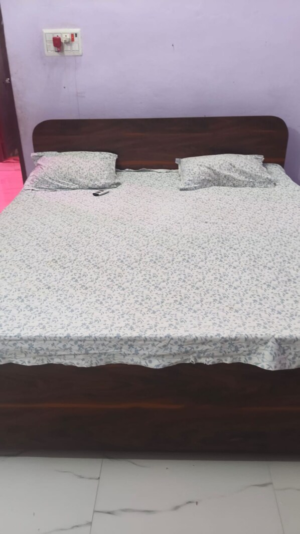 A bed with a floral bedspread, a wooden headboard, and a wall socket.