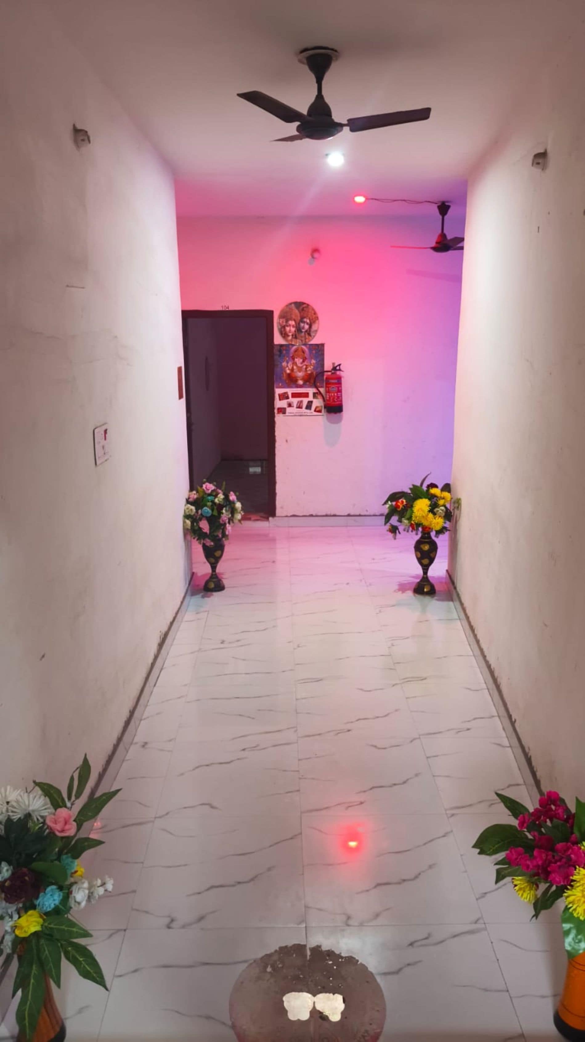A hallway with a ceiling fan, a fire extinguisher, and two flower arrangements.