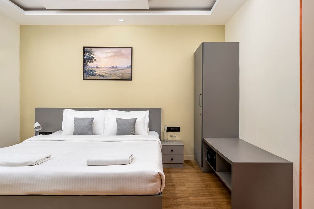A hotel room with a bed, bedside table, lamp, and a painting on the wall.