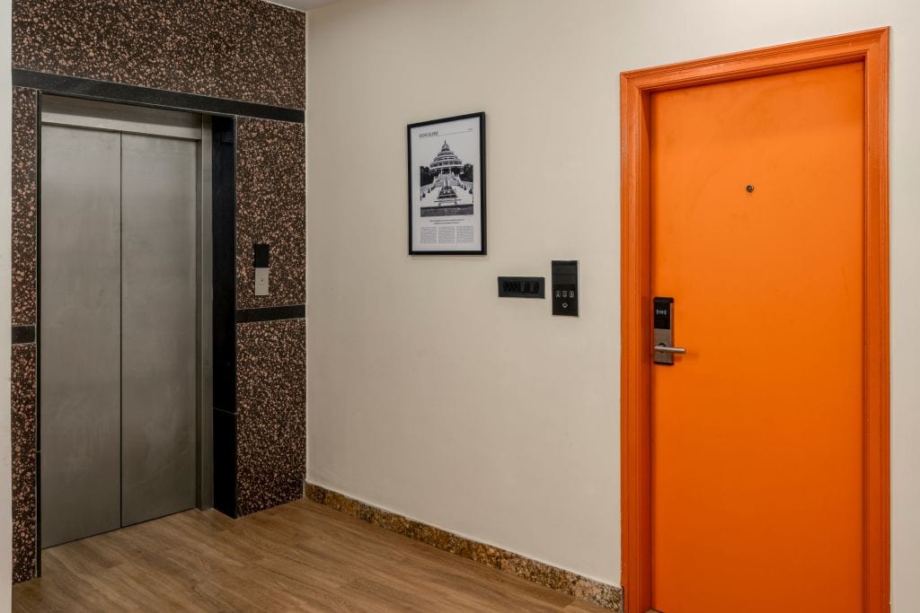 An elevator, a framed picture on the wall, and an orange door.