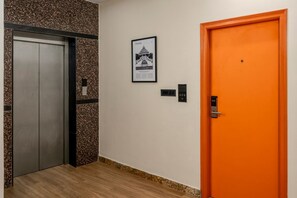 An elevator, a framed picture on the wall, and an orange door. - Wandr Hotel Koramangala (Bengaluru)