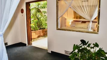 Quarto com cama, janela com vista para o verde, planta em vaso e porta que dá para o exterior.